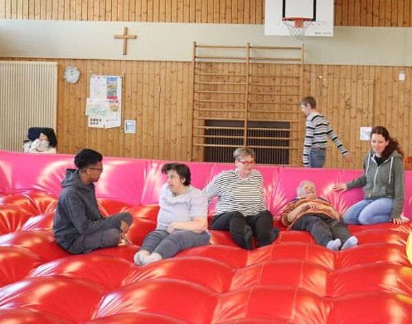 Eine Gruppe Menschen sitzt oder liegt auf einem riesigen aufgeblasenen Kissen